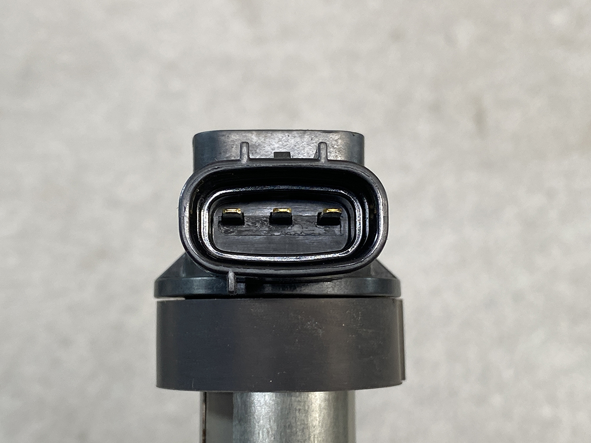 SUZ-COIL-NL2_4 SUZUKI Genuine IGNITION COIL DENSO NL2 099700 / R06A, K6A Engine » NZ.95 » JDM-PARTS NZ » JDM-PARTS NZ Close-up of a three-pin automotive electrical connector with a black plastic housing, mounted on a metallic rod against a gray background. SUZUKI Genuine IGNITION COIL DENSO NL2 099700 / R06A, K6A Engine » JDM-PARTS NZ