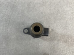 Top-down view of a small cylindrical sensor with a central bore and a mounting lug, labeled A16, on a gray surface.