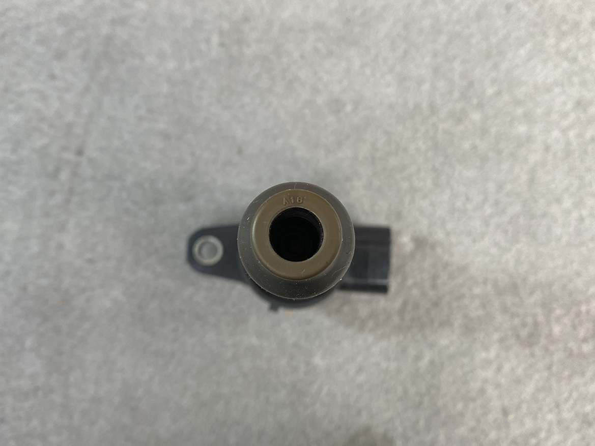 SUZ-COIL-NL2_6 SUZUKI Genuine IGNITION COIL DENSO NL2 099700 / R06A, K6A Engine » NZ.95 » JDM-PARTS NZ » JDM-PARTS NZ Top-down view of a small cylindrical sensor with a central bore and a mounting lug, labeled A16, on a gray surface. SUZUKI Genuine IGNITION COIL DENSO NL2 099700 / R06A, K6A Engine » JDM-PARTS NZ