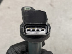 Close-up of a black automotive sensor with a 6-pin electrical connector and exposed gold contacts.