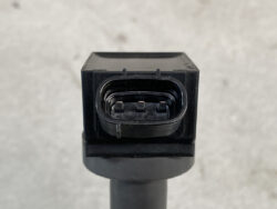 Close-up of a black automotive electrical connector with three metal pins inside a rectangular receptacle on a sensor lead