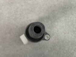 Close-up of a cylindrical automotive sensor connector with a central bore and rubber seal on a mounting bracket, viewed from above.