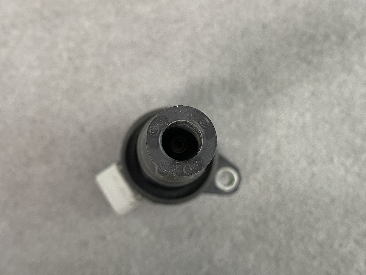 TOY-COIL-B2050_5 TOYOTA / DAIHATSU Genuine IGNITION COIL / 19500-B2050 / KF Engine » NZ.95 » JDM-PARTS NZ » JDM-PARTS NZ Close-up of a cylindrical automotive sensor connector with a central bore and rubber seal on a mounting bracket, viewed from above. TOYOTA / DAIHATSU Genuine IGNITION COIL / 19500-B2050 / KF Engine » JDM-PARTS NZ