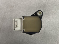 Automotive engine sensor with a white electrical connector on the left and a mounting hole on the right side.
