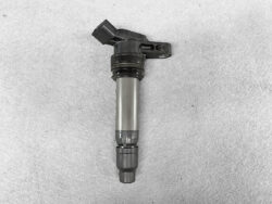 Automotive ignition coil with electrical connector and spark plug boot lying on a gray surface