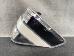 Tail light assembly for a car, featuring clear lens and chrome/black trim, photographed on a dark surface.