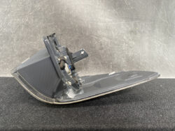 Detached gray car tail light housing with mounting bracket and wiring, resting on a dark surface