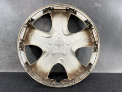 Beige plastic Toyota wheel cover with five spokes and central Toyota logo, lying on a dark surface.