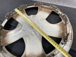 Circular beige plastic car wheel cover with a tape measure laid diagonally across it, showing a diameter of about 38 cm (roughly 15 inches).