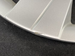 Close-up of a silver metal surface with a small dent and chipped edge against a dark background, likely a worn or damaged part.