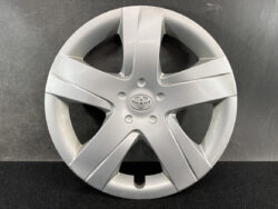 Silver Toyota wheel cover with five spokes and a central logo, resting on a dark background.