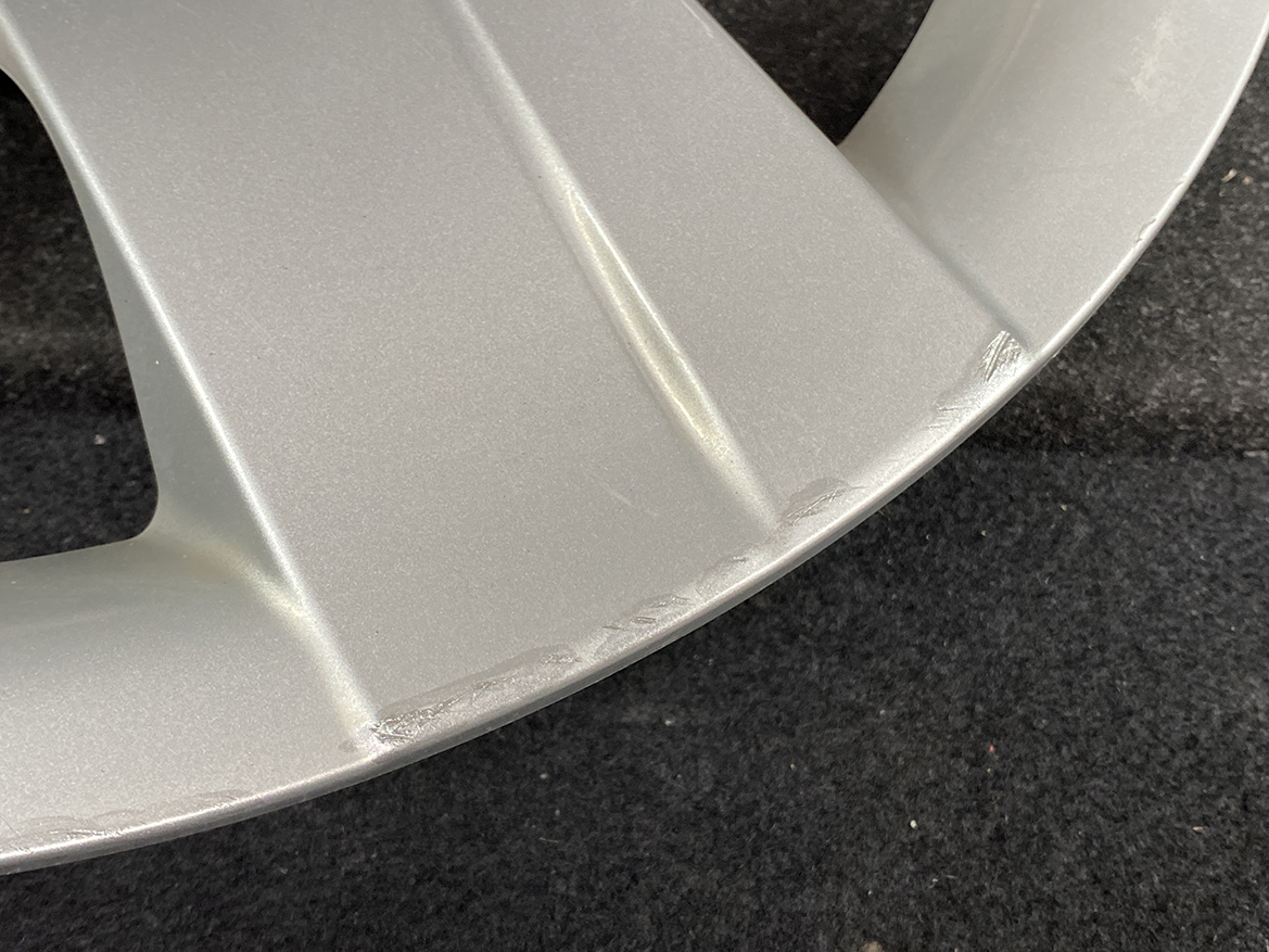 B392_6 TOYOTA RACTIS NSP120, NCP120 Genuine 16inch WHEEL CAP / HUB CAP 42602-52460 » NZ.95 » JDM-PARTS NZ » JDM-PARTS NZ Close-up of a silver metallic surface with light scratches along a curved edge on a dark fabric background. TOYOTA RACTIS NSP120, NCP120 Genuine 16inch WHEEL CAP / HUB CAP 42602-52460 » JDM-PARTS NZ