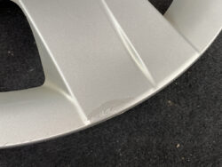 Close-up of a silver metallic car part with a small surface scuff along the curved edge.