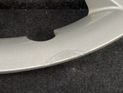 Close-up of a silver curved metal surface with a scrape and scuff marks near a notch, on a dark background.