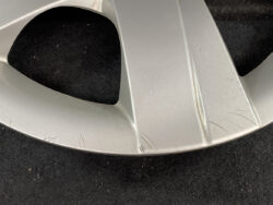 Close-up of a silver alloy wheel rim with several scratches along the outer lip against a dark background