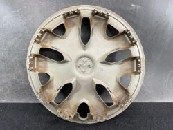 Beige circular car wheel hubcap with eight spokes laid flat on a dark surface.