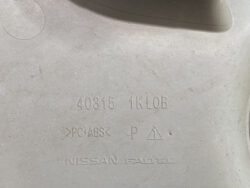 Close-up of a light gray plastic car part with molded markings: part number 40315 1K0B, PC+ABS, Nissan Parts, and recycling/pictogram symbols visible.