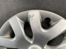 Silver car hubcap with several scratches and scuff marks on its surface.