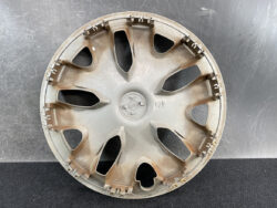 Circular car wheel hubcap with multiple curved spokes, dusty brown staining, resting on a dark surface