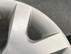 Close-up of a scratched silver car wheel cover with angular spokes and a circular cutout.