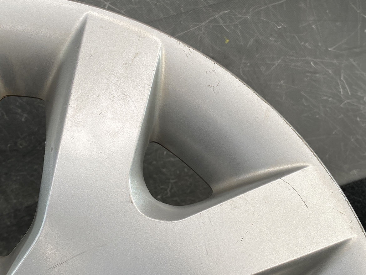B399_6 NISSAN LEAF AZE0 Genuine 16inch WHEEL CAP / HUB CAP 40315 1KL0B x1 » NZ.95 » JDM-PARTS NZ » JDM-PARTS NZ Close-up of a scratched silver car wheel cover with angular spokes and a circular cutout. NISSAN LEAF AZE0 Genuine 16inch WHEEL CAP / HUB CAP 40315 1KL0B x1 » JDM-PARTS NZ