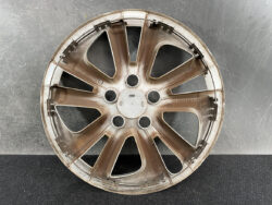 Brown alloy car wheel rim with eight spokes resting on a dark, textured surface
