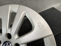Silver alloy car wheel with Toyota center cap, showing surface scratches and scuff marks on the rim edge.