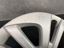 Close-up of a silver alloy wheel rim with surface scratches and scuffs on a dark background, showing curved spokes nearby.
