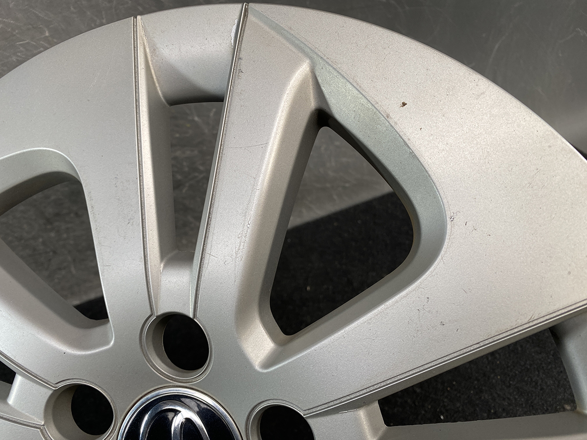 B402_8 TOYOTA PRIUS ZVW50 ZVW51 Genuine 15inch WHEEL CAP / HUB CAP » NZ.95 » JDM-PARTS NZ » JDM-PARTS NZ Close-up of a silver alloy wheel rim with a scratched outer edge and minor dents; center emblem partially visible. TOYOTA PRIUS ZVW50 ZVW51 Genuine 15inch WHEEL CAP / HUB CAP » JDM-PARTS NZ