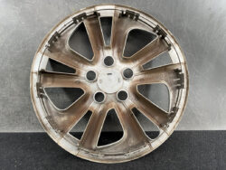 Dusty car alloy wheel rim with eight spokes, circular center cap, and lug nut holes visible against a dark backdrop