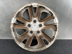 Brown alloy car wheel rim without a tire, showing a ten-spoke design and center hub, resting on a dark textured surface.