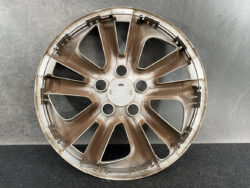 Brown alloy car wheel rim with multiple spokes lying on a dark surface, center hub visible, dusty and used-looking.