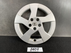 Silver Toyota wheel cover with five spokes and the Toyota emblem in the center, standing upright on a dark surface.