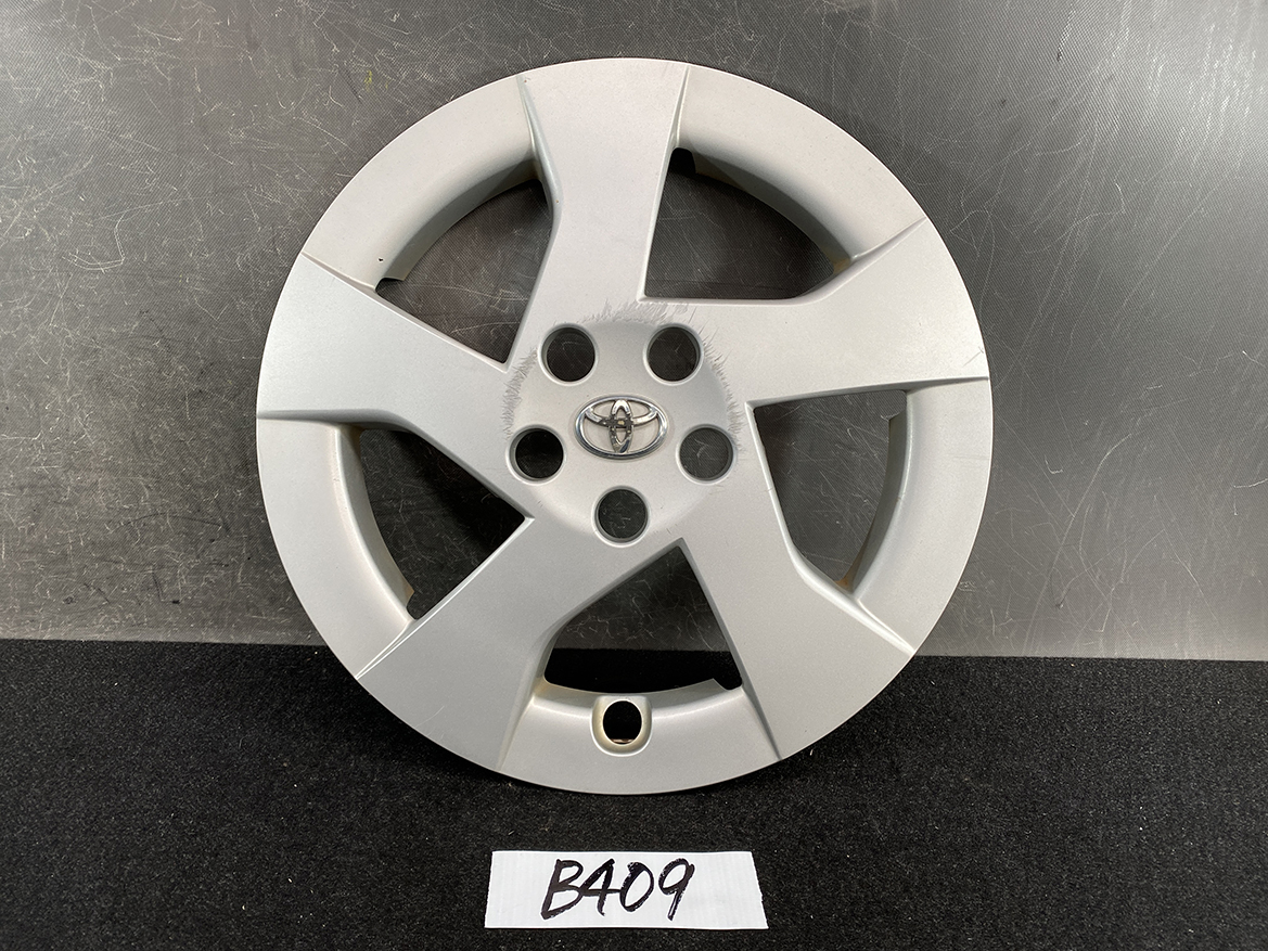 B409_1 TOYOTA PRIUS ZVW30 ZVW35 Genuine 15inch WHEEL CAP / HUB CAP » NZ.95 » JDM-PARTS NZ » JDM-PARTS NZ Silver Toyota wheel cover with five spokes and the Toyota emblem in the center, standing upright on a dark surface. TOYOTA PRIUS ZVW30 ZVW35 Genuine 15inch WHEEL CAP / HUB CAP » JDM-PARTS NZ
