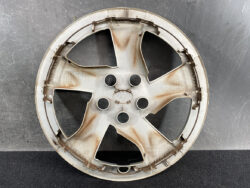 Rusty five-spoke alloy car wheel rim resting on a dark surface, with dirt and grime on the spokes.