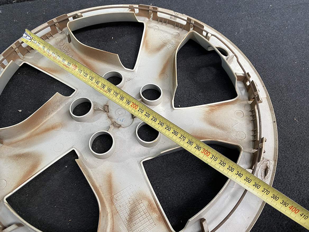 B409_4 TOYOTA PRIUS ZVW30 ZVW35 Genuine 15inch WHEEL CAP / HUB CAP » NZ.95 » JDM-PARTS NZ » JDM-PARTS NZ Beige plastic car wheel hubcap with rust stains lying on dark pavement; a yellow measuring tape runs diagonally across it, showing about 0–400 mm. TOYOTA PRIUS ZVW30 ZVW35 Genuine 15inch WHEEL CAP / HUB CAP » JDM-PARTS NZ