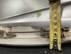 Close-up of a yellow measuring tape held against a circular metal vent/fan housing, showing about 60 cm tallened measurement.