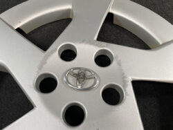 Silver Toyota alloy wheel hub with the emblem, showing scuff marks around the center area and five lug holes.