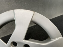Close-up of a silver car alloy wheel rim with scratches and small edge dents nearby on a dark floor surface.