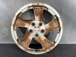 Brown car alloy wheel rim with five curved spokes resting on a gray wall surface