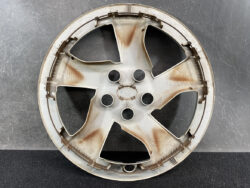 Rusty five-spoke car wheel rim resting on a dark surface against a gray background.