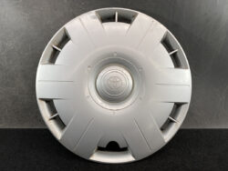 Silver Toyota hubcap laid flat with a central Toyota emblem and radiating grooves against a dark background.