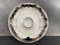 Round Toyota hubcap with central emblem, dirty and scuffed, resting on a dark surface.
