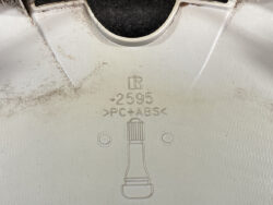 Close-up of a light gray plastic panel showing the material code PC+ABS, a part number 0.2595, and a bottle icon with two circular holes nearby.