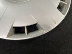 Close-up of a silver alloy wheel with a chipped edge and rust stains along the rim around a damaged section
