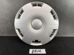 Silver Toyota hubcap/wheel center cap with a circular emblem resting on a dark surface, featuring radial grooves and cutouts around the edge.