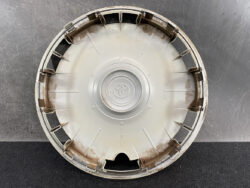 Front view of a dusty Toyota hubcap/center cap with spokes and inner circle, resting on a dark surface.