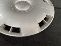 Close-up of a silver Toyota wheel hubcap with visible scratches and scuffs along the lower edge on a dark carpeted surface