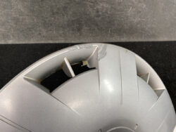 Close-up of a gray circular plastic cover with a broken vent tab and surface scratches.