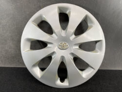 Silver Toyota hubcap with emblem and eight curved spokes, lying on a dark surface